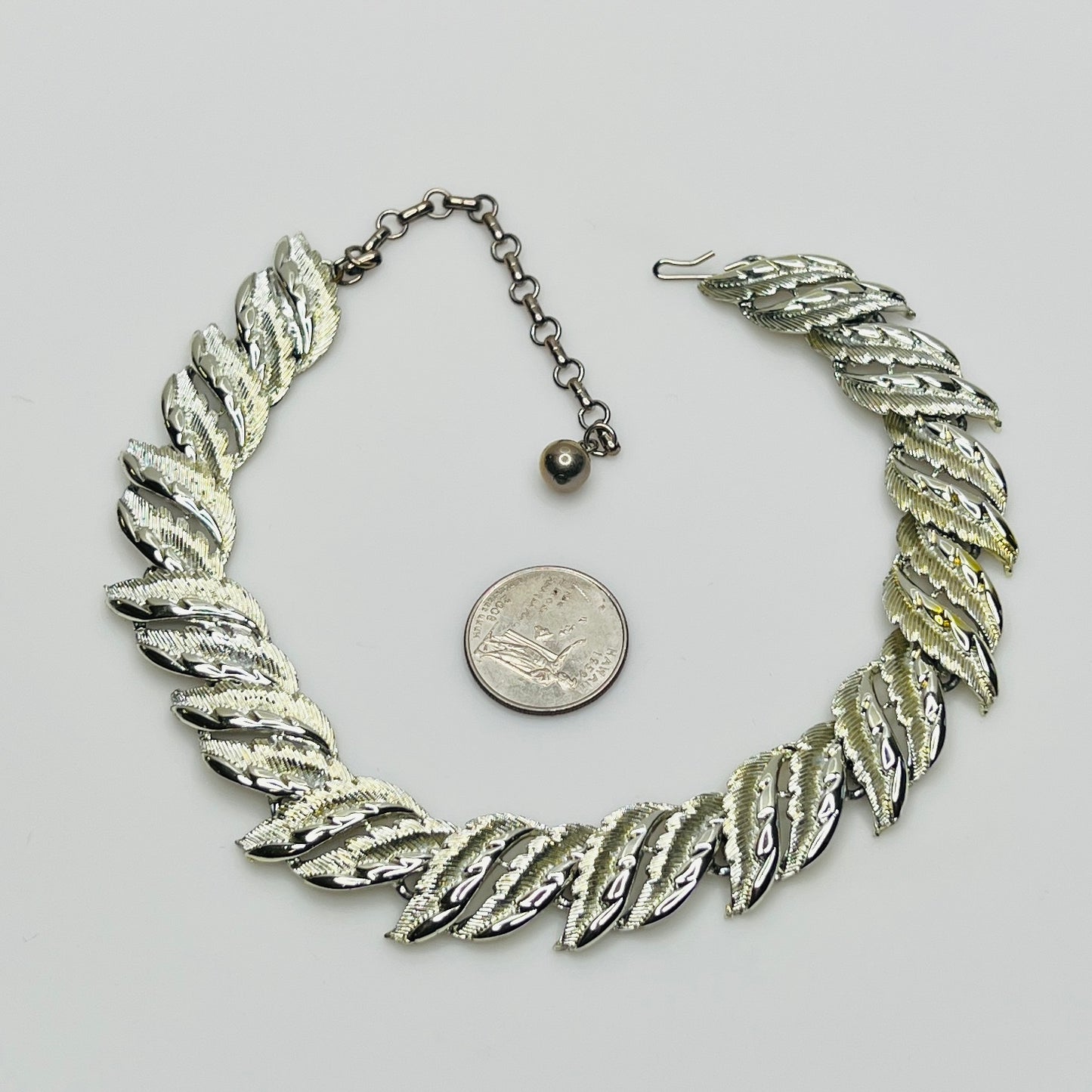 Silver leaf necklace with a quarter for scale on a light gray background