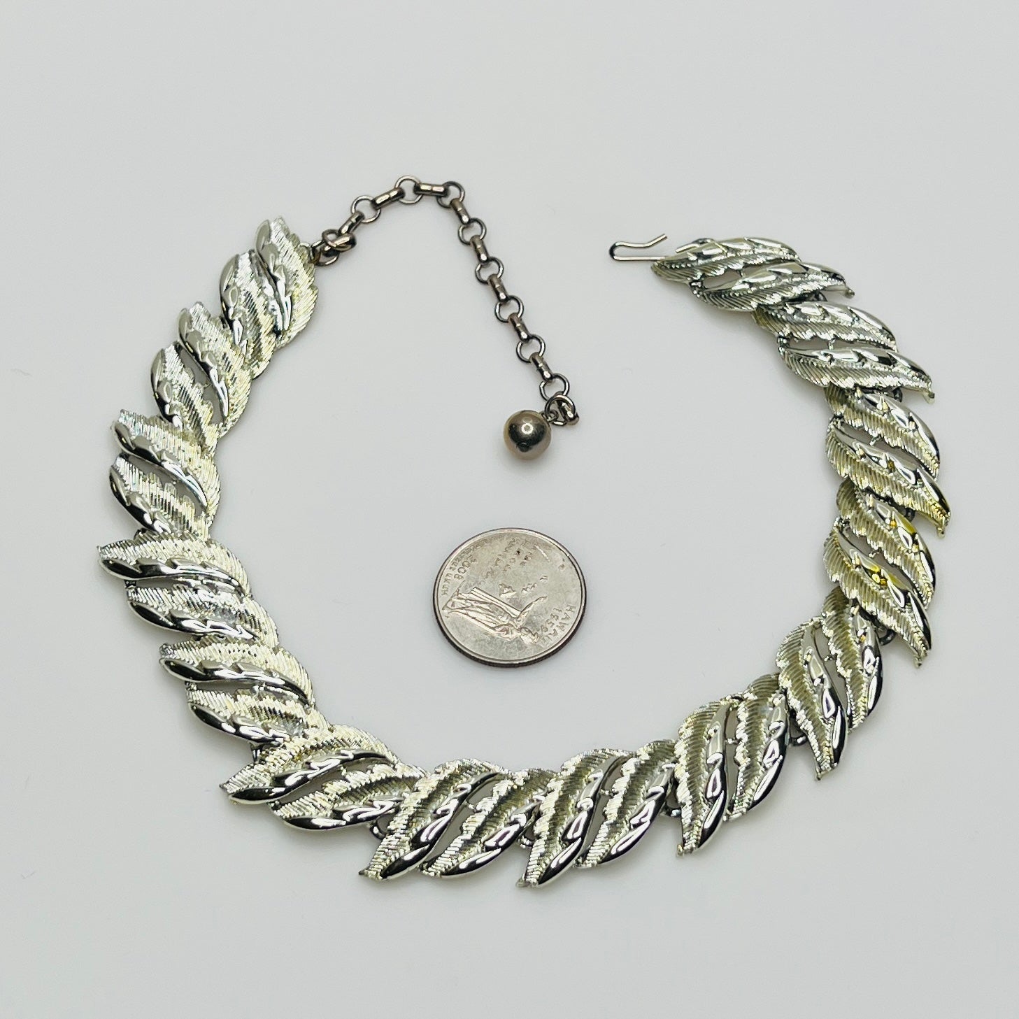 Silver leaf necklace with a quarter for scale on a light gray background