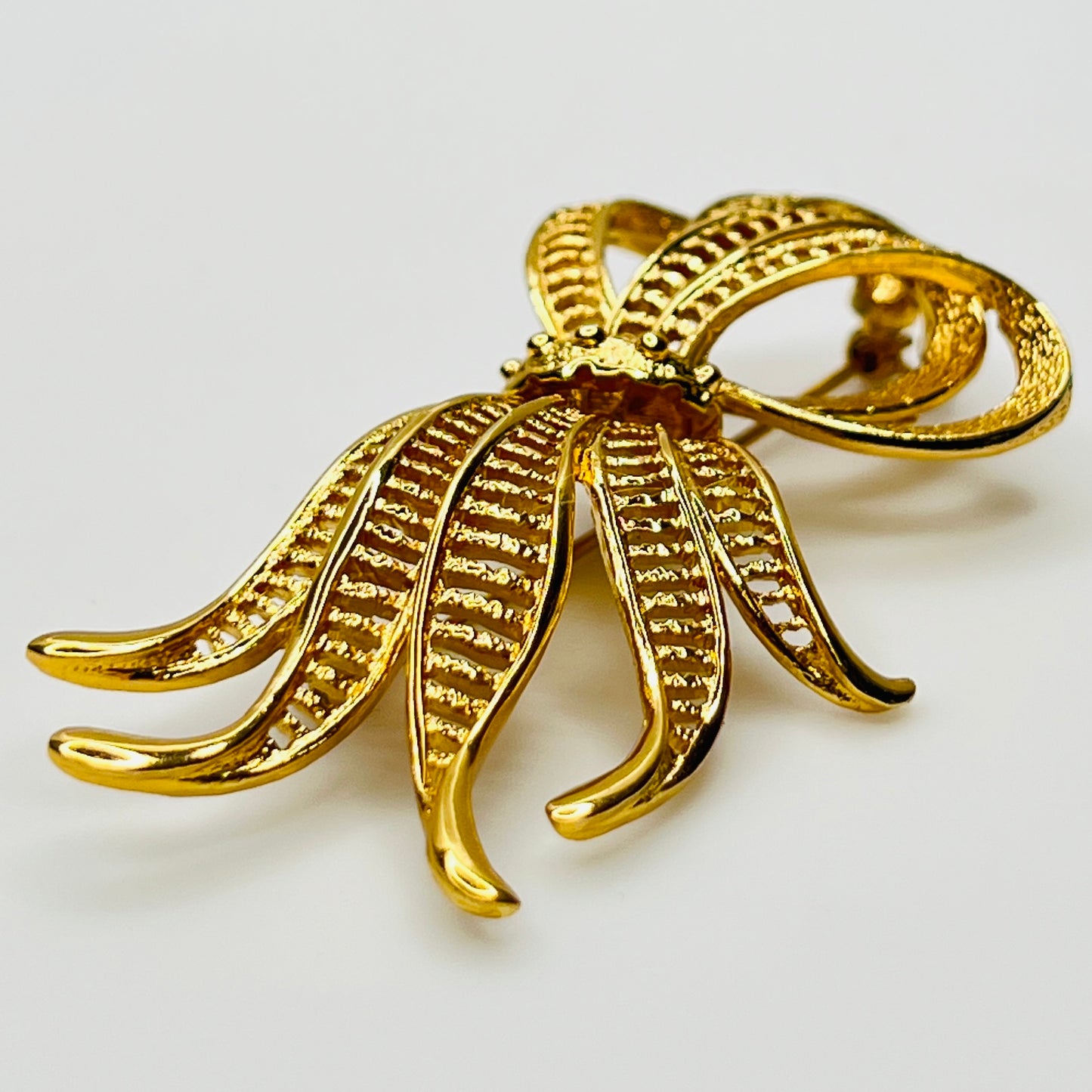 Side view of dimensional gold ribbon brooch with textured detailing