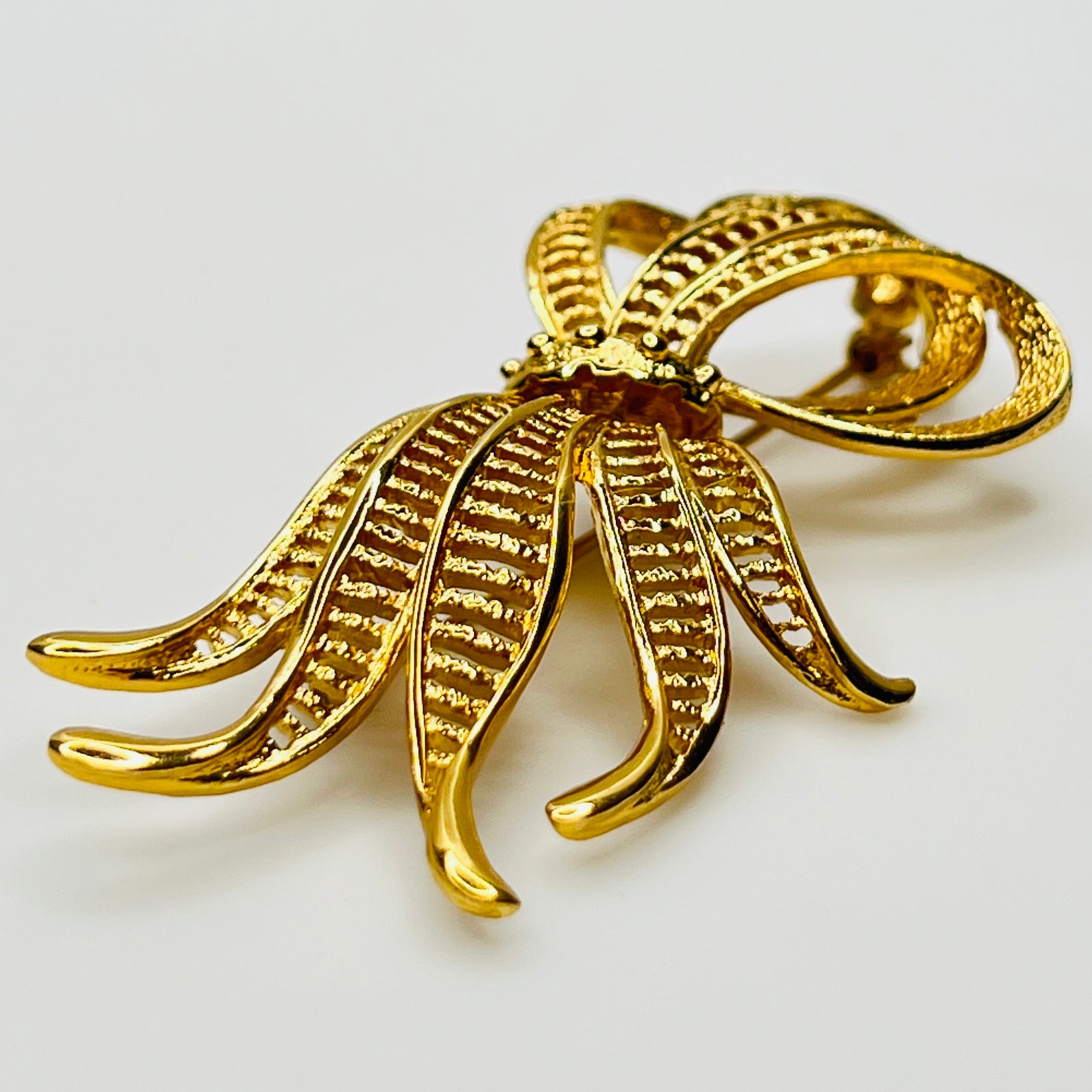 Side view of dimensional gold ribbon brooch with textured detailing