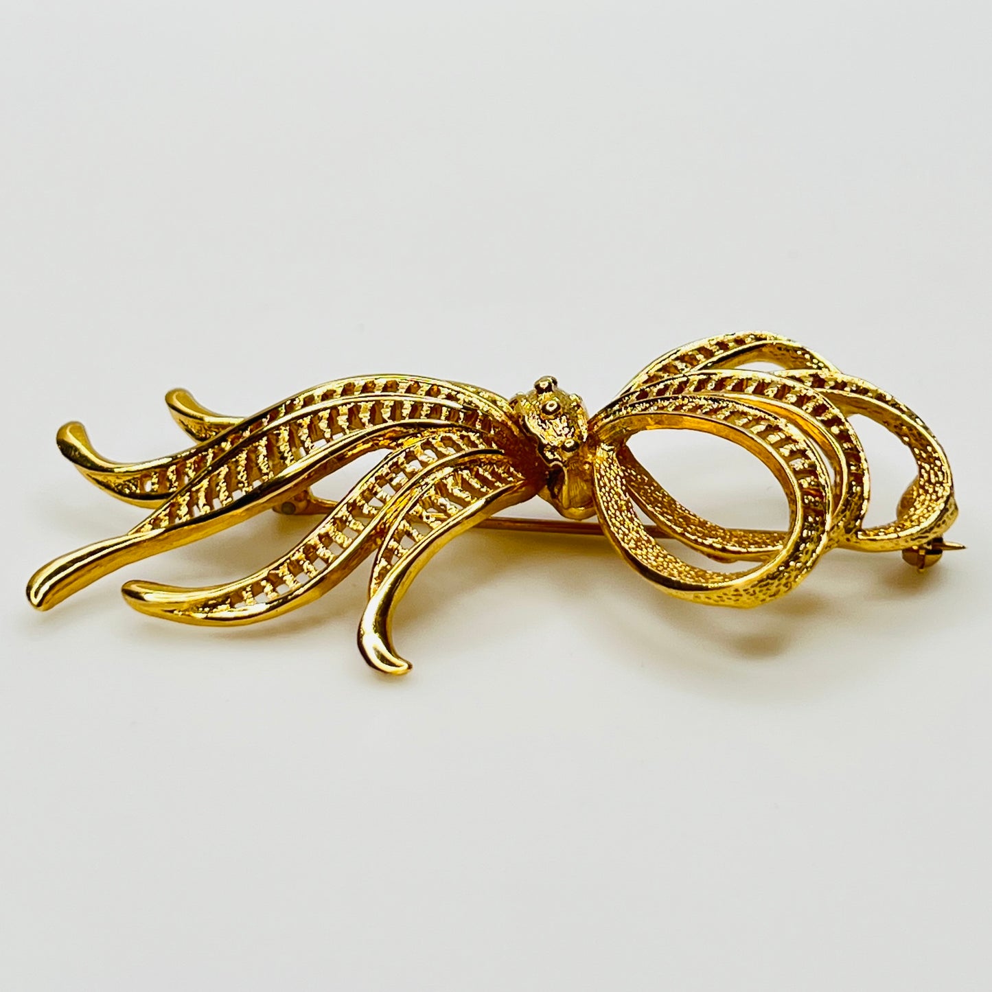Side view of dimensional gold ribbon brooch with textured detailing