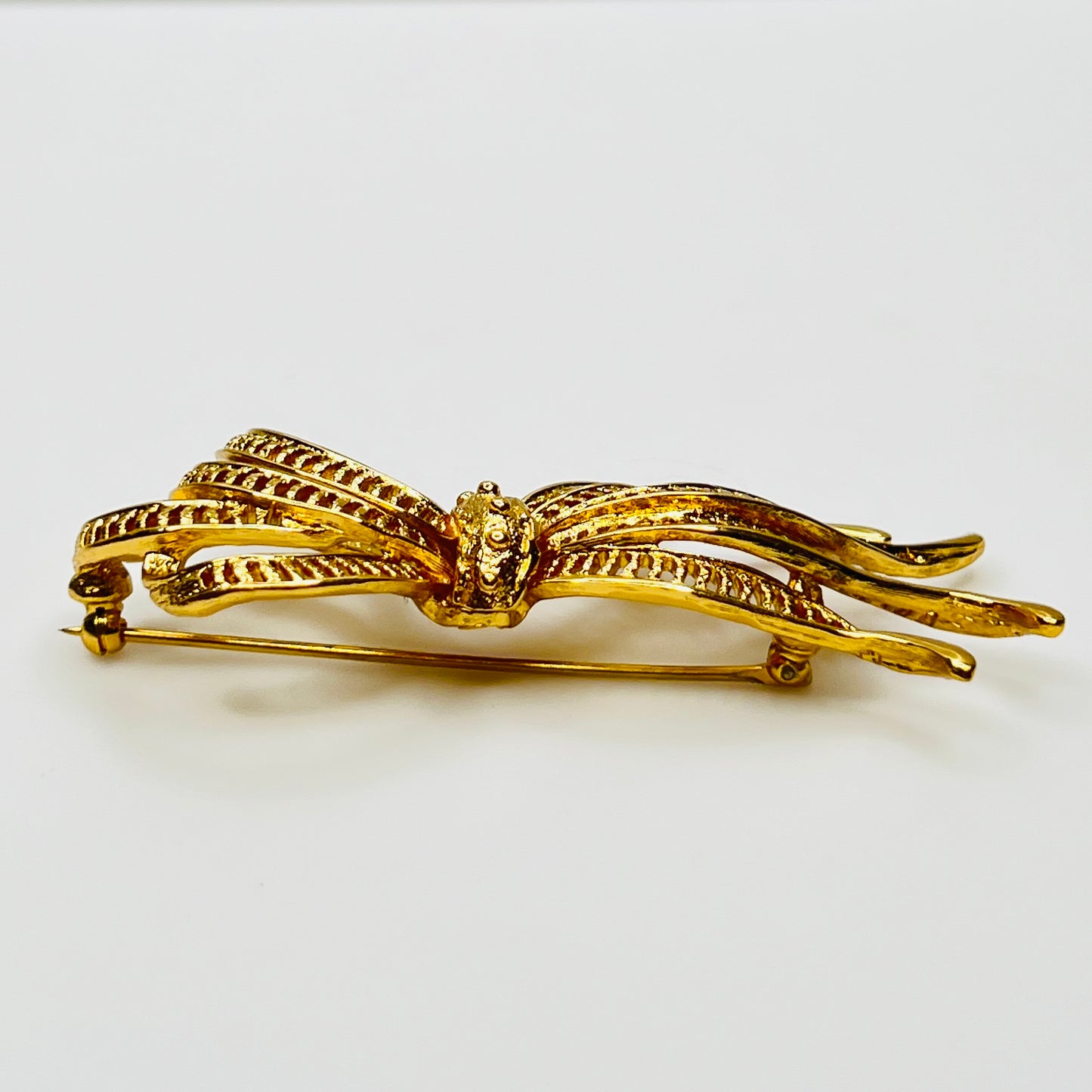 Side view of dimensional gold ribbon brooch with textured detailing