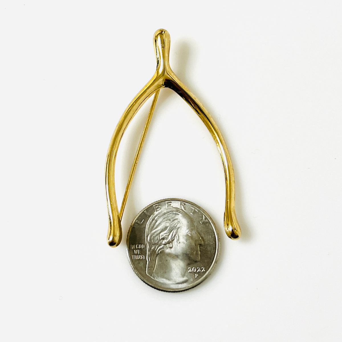 Napier gold-tone wishbone brooch beside a quarter, showing its 2¼-inch length and open design.