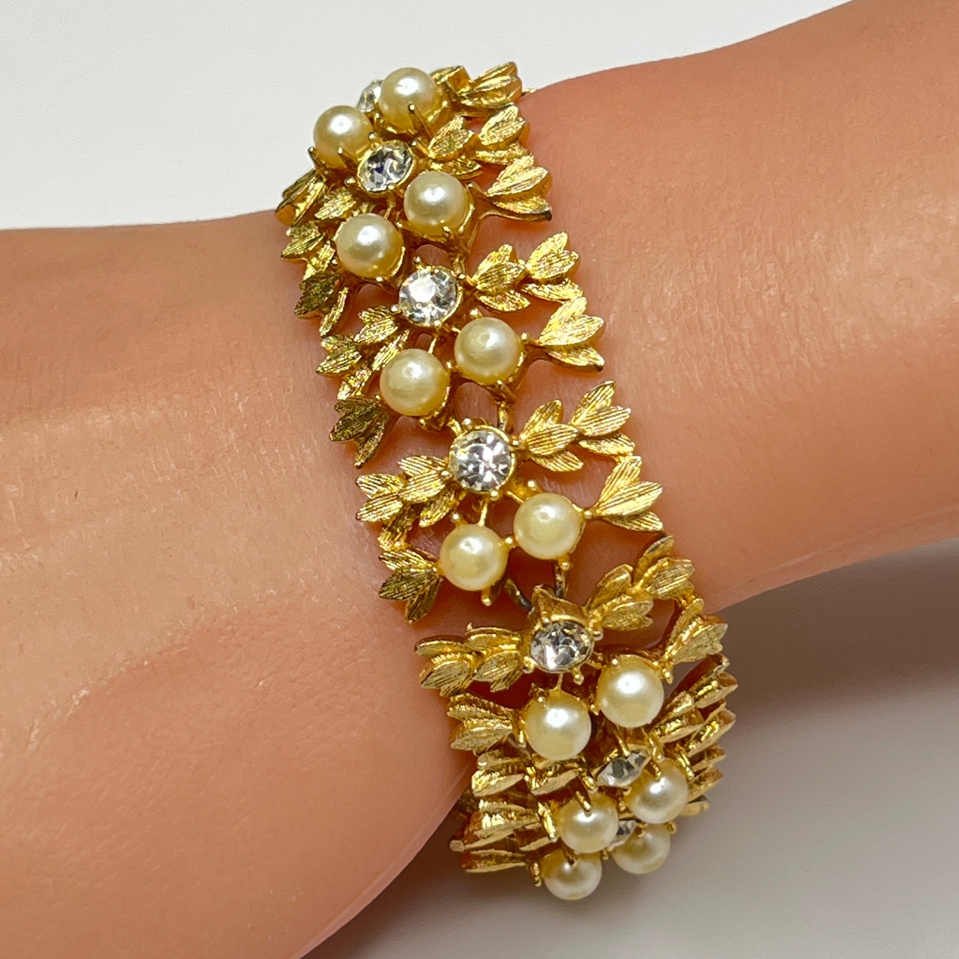 Gold bracelet with pearls and crystals on a wrist against a white background