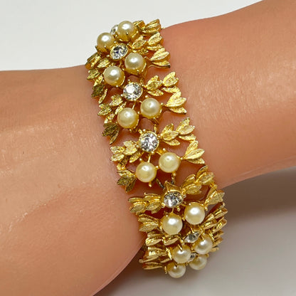 Gold bracelet with pearls and crystals on a wrist against a white background
