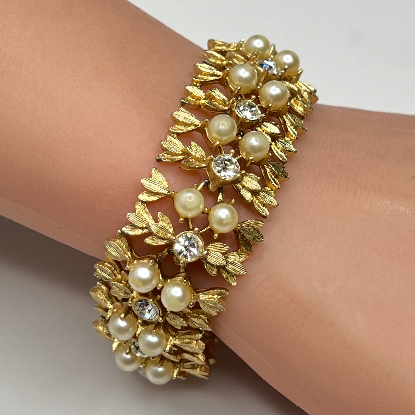 Gold bracelet with pearls and crystals on a wrist against a neutral background