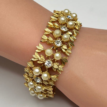 Gold bracelet with pearls and crystals on a wrist against a neutral background