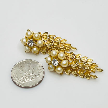 Gold earrings with pearls and crystals next to a quarter on a white background