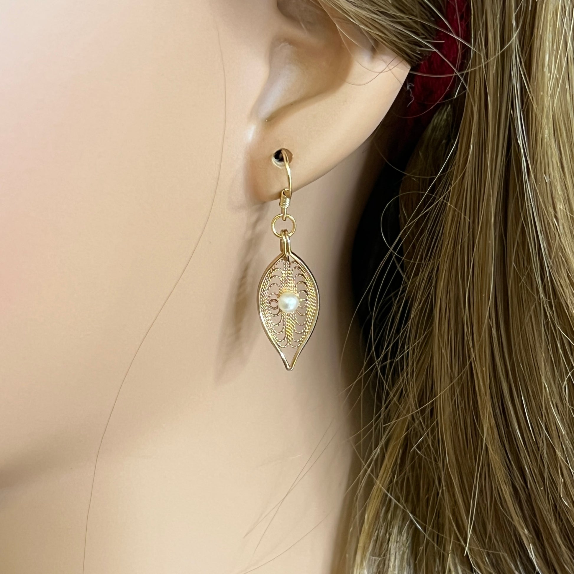 Close-up of gold-tone openwork earrings featuring pearl centers