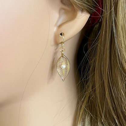 Close-up of gold-tone openwork earrings featuring pearl centers