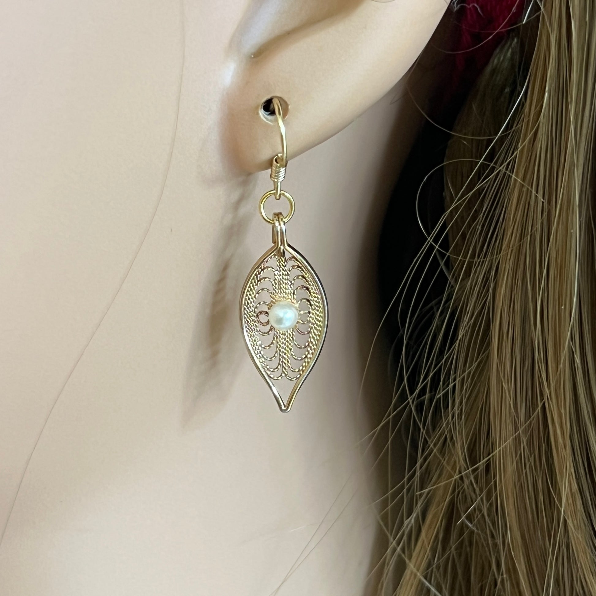 Close-up of gold-tone openwork earrings featuring pearl centers