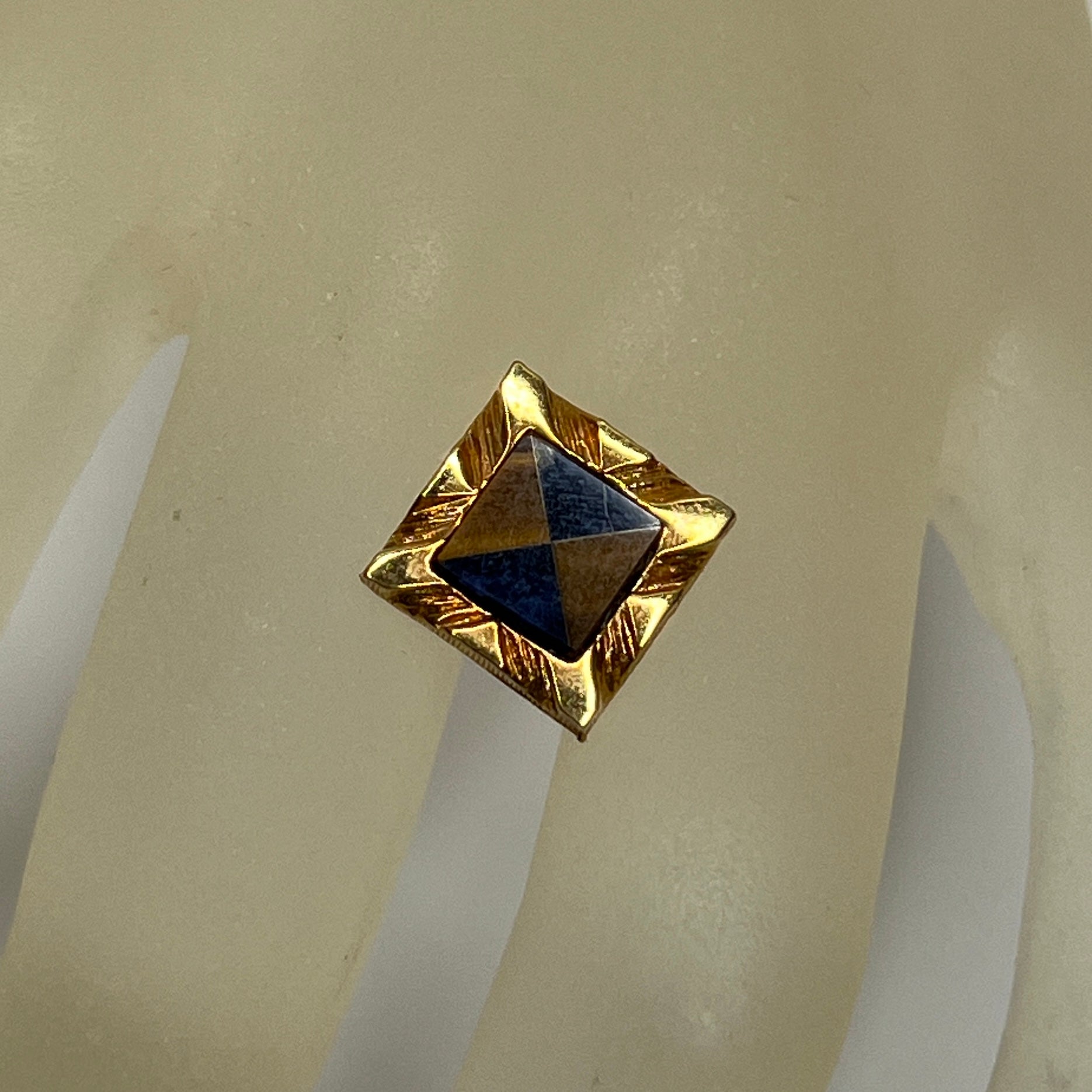 Close-up of Karatclad gold tie pin with navy and brown stone inlay