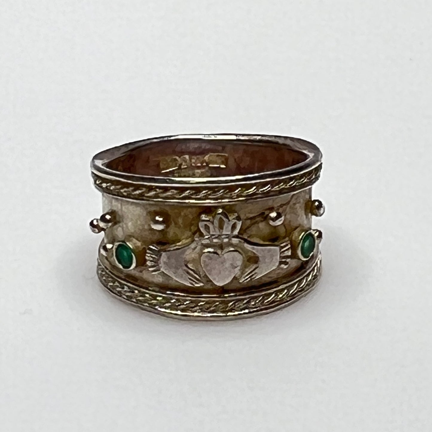 Close-up of Claddagh motif and emerald accent on wide silver ring