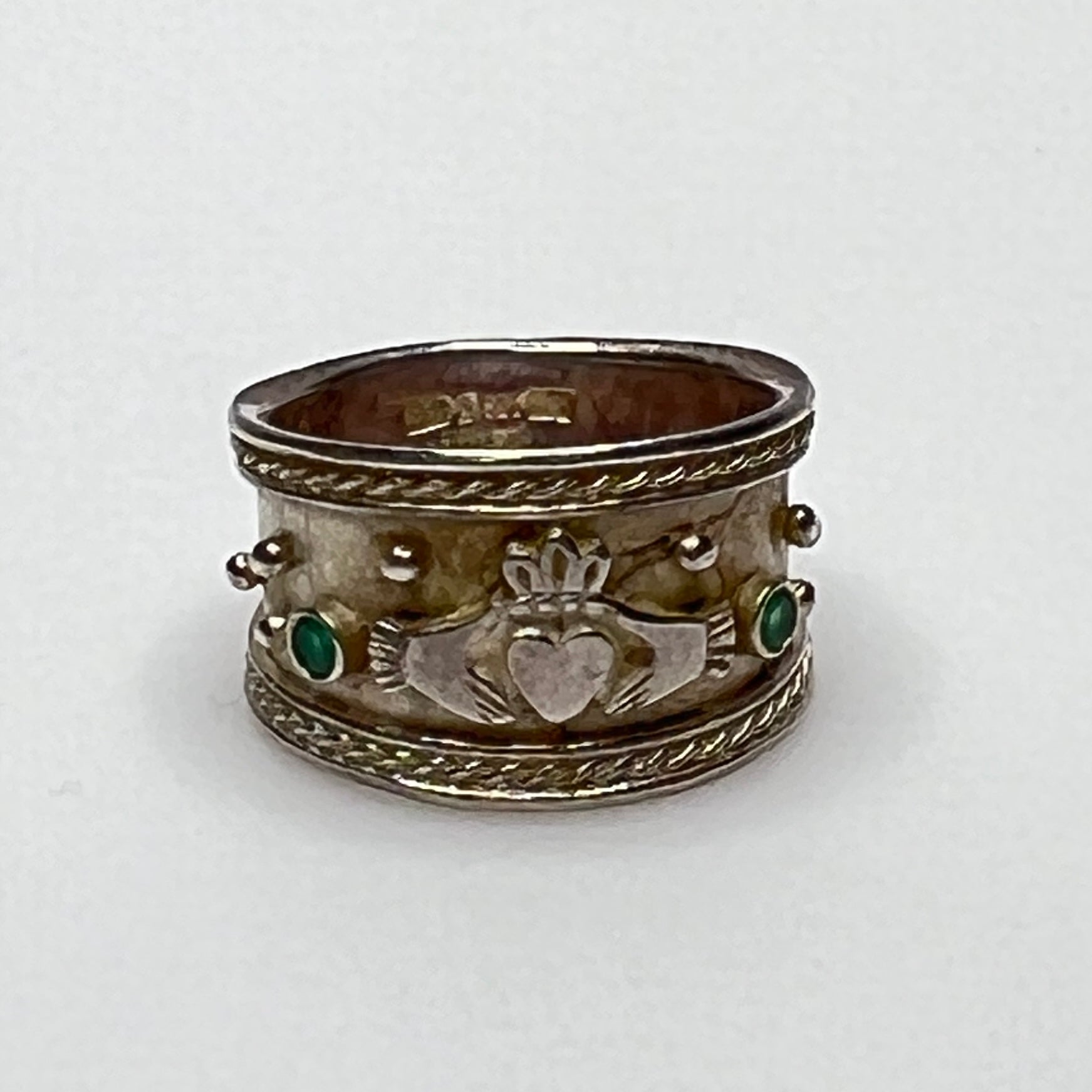 Close-up of Claddagh motif and emerald accent on wide silver ring