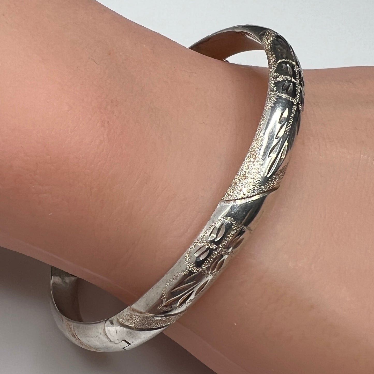 Sterling silver oval bangle shown on wrist with polished floral etching