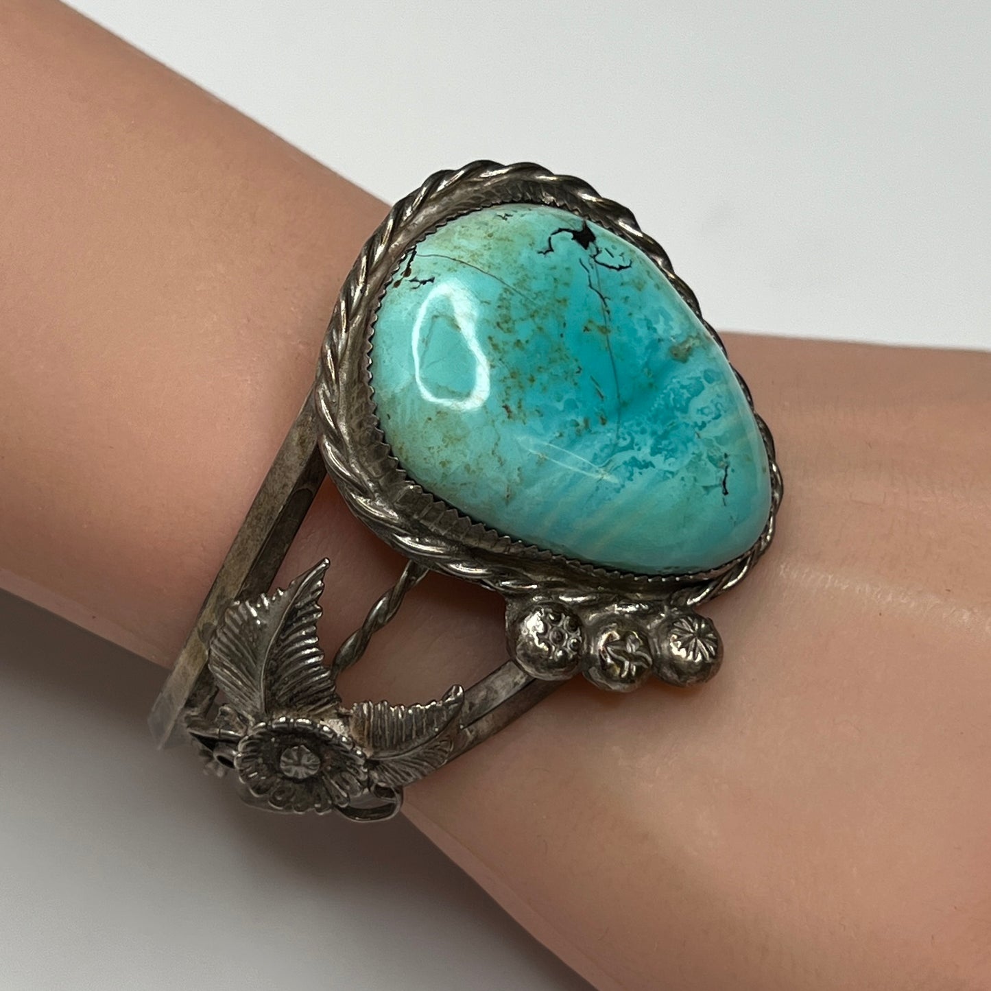 Angled view showing detailed flower and feather silverwork on vintage turquoise cuff
