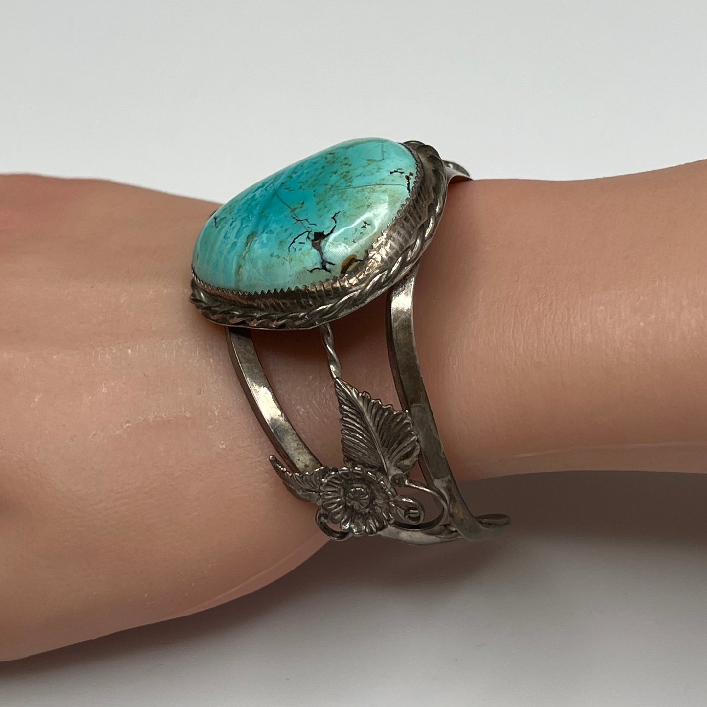 Angled view showing detailed flower and feather silverwork on vintage turquoise cuff