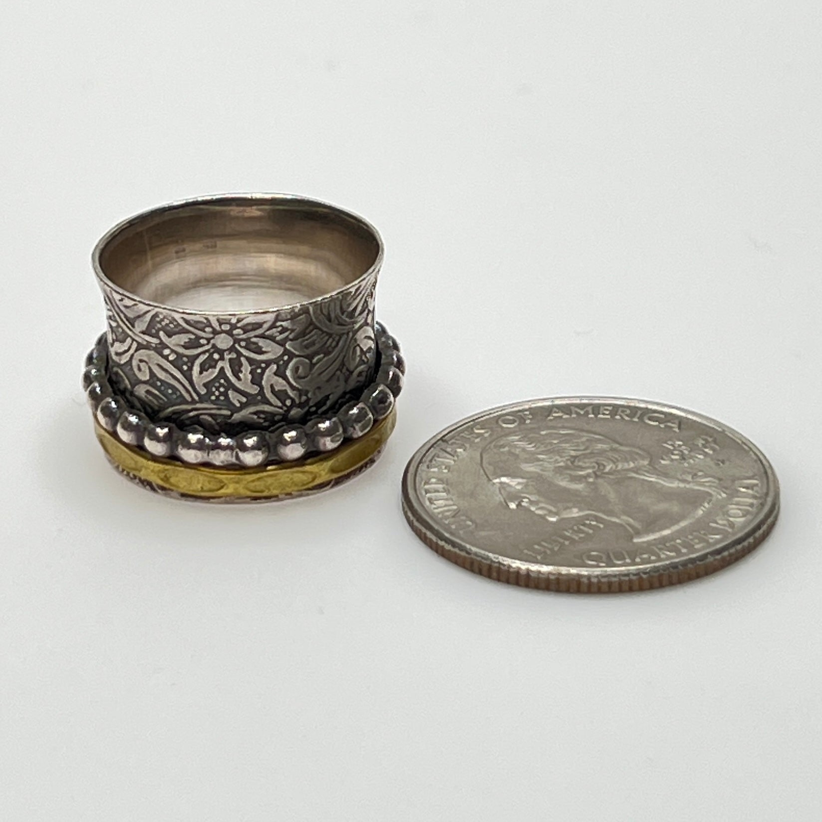 Wide sterling silver spinner ring with floral embossing, brass band, and beaded spinner