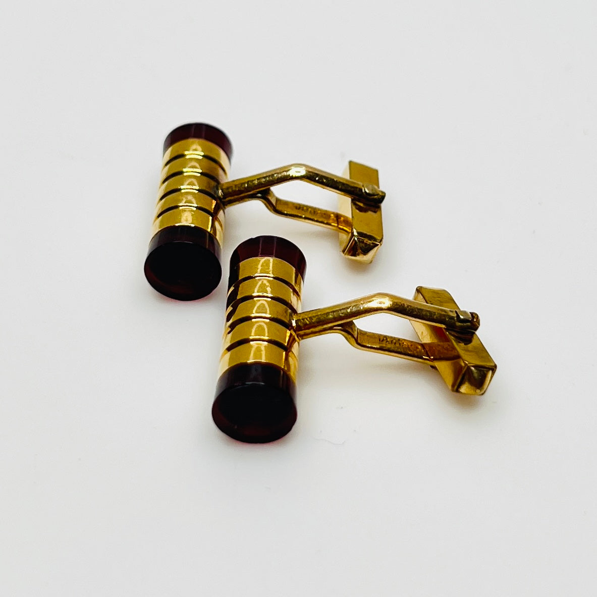 Close-up of cylindrical cufflinks with grooved goldtone design and red ends