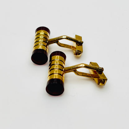 Close-up of cylindrical cufflinks with grooved goldtone design and red ends