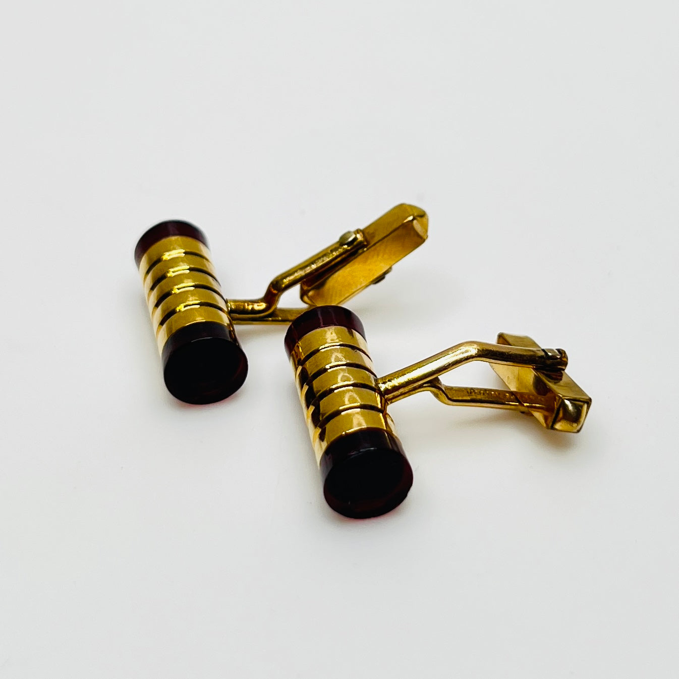 Close-up of cylindrical cufflinks with grooved goldtone design and red ends