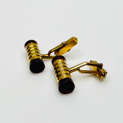 Close-up of cylindrical cufflinks with grooved goldtone design and red ends