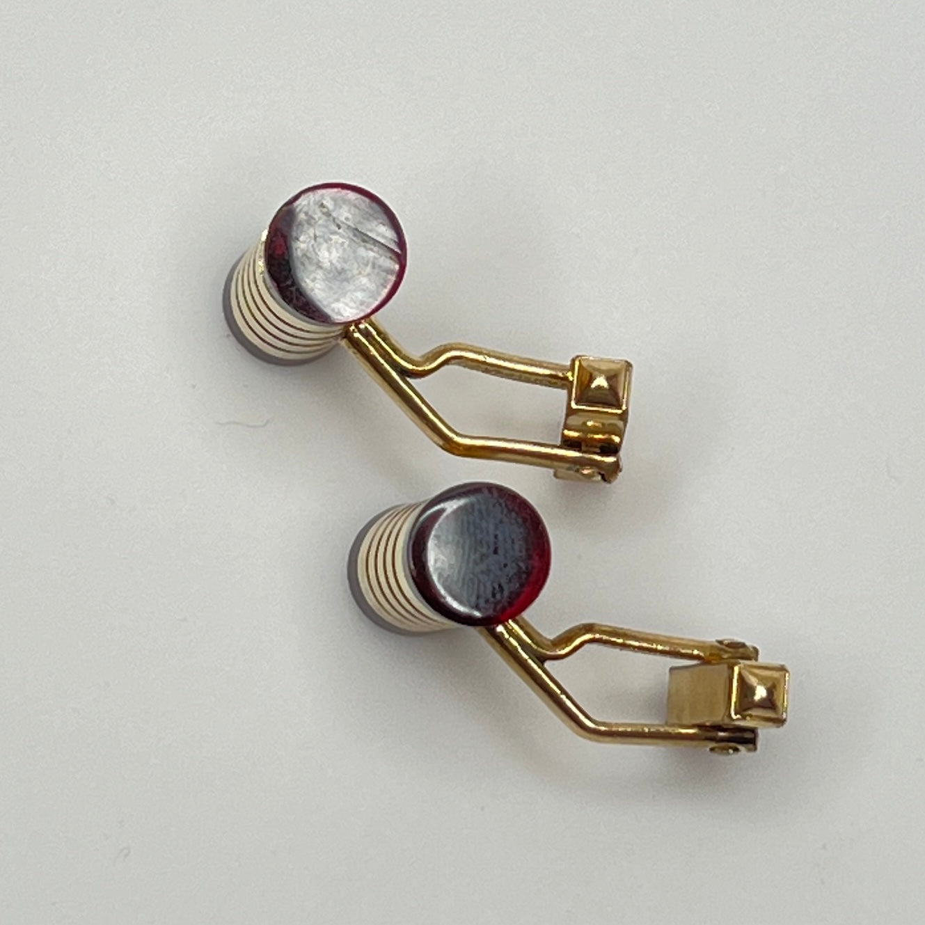 Close-up of cylindrical cufflinks with grooved goldtone design and red ends