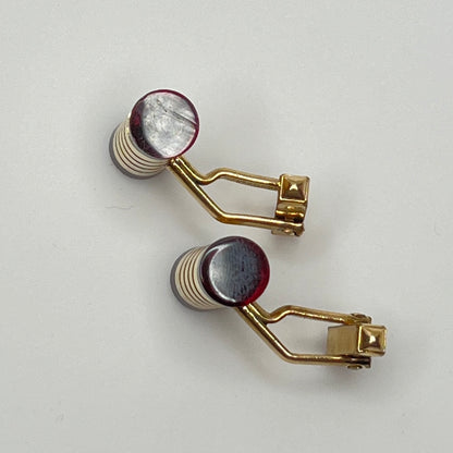 Close-up of cylindrical cufflinks with grooved goldtone design and red ends
