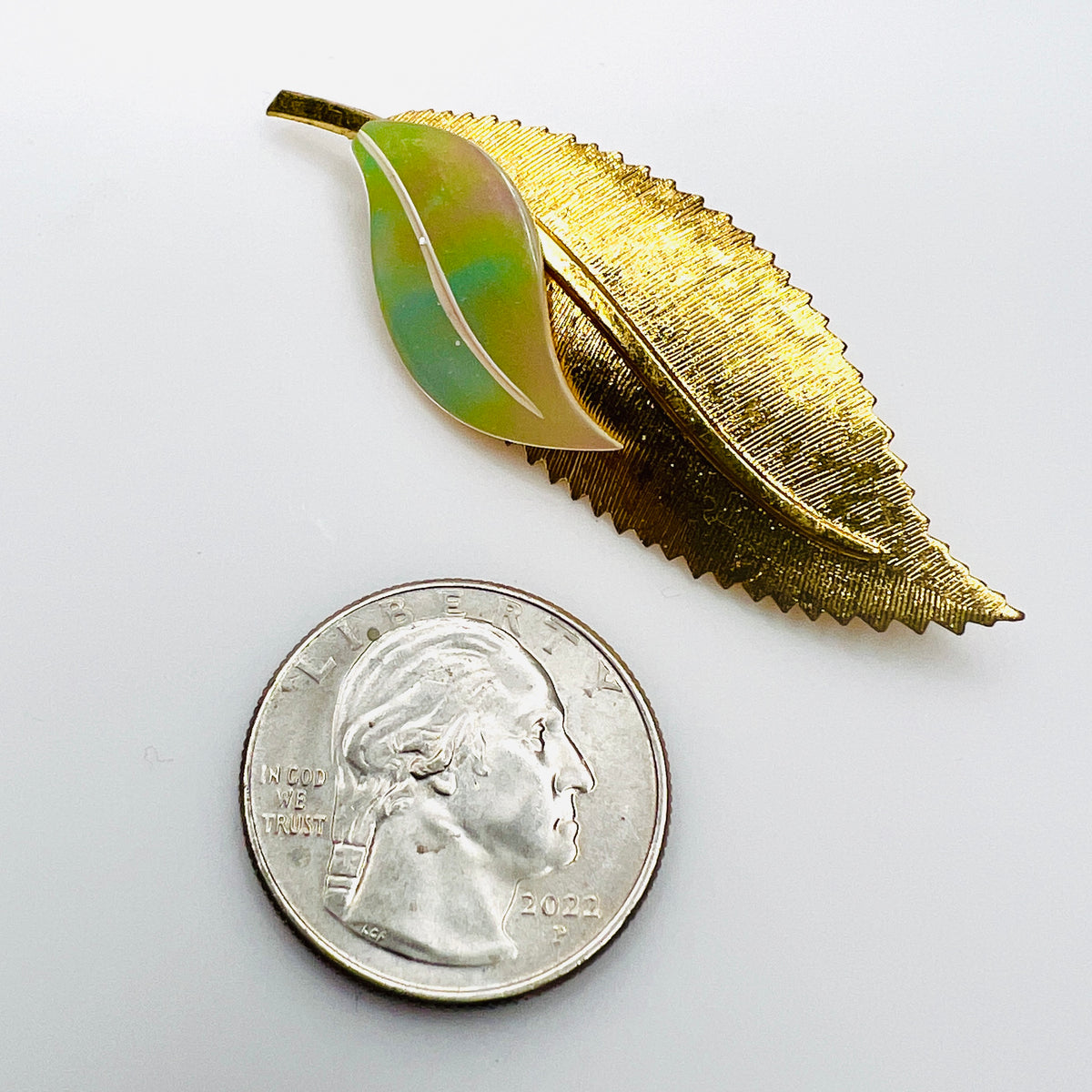 West German vintage gold leaf brooch with green and ivory mother of pearl beside a quarter for size comparison.
