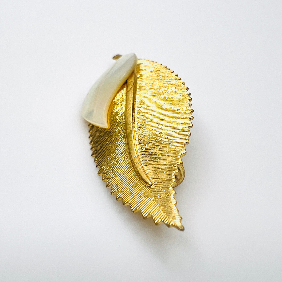Side view of vintage 1950s gold-tone botanical brooch showing raised mother of pearl leaf and dimensional metal construction.