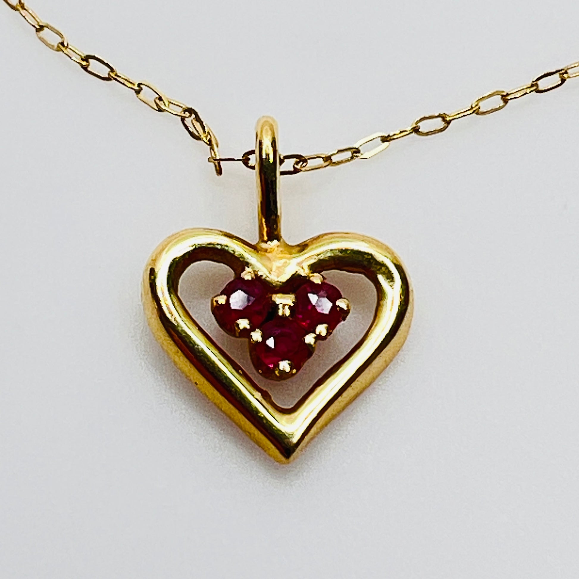 Close up ruby heart pendant three stone cluster gold setting