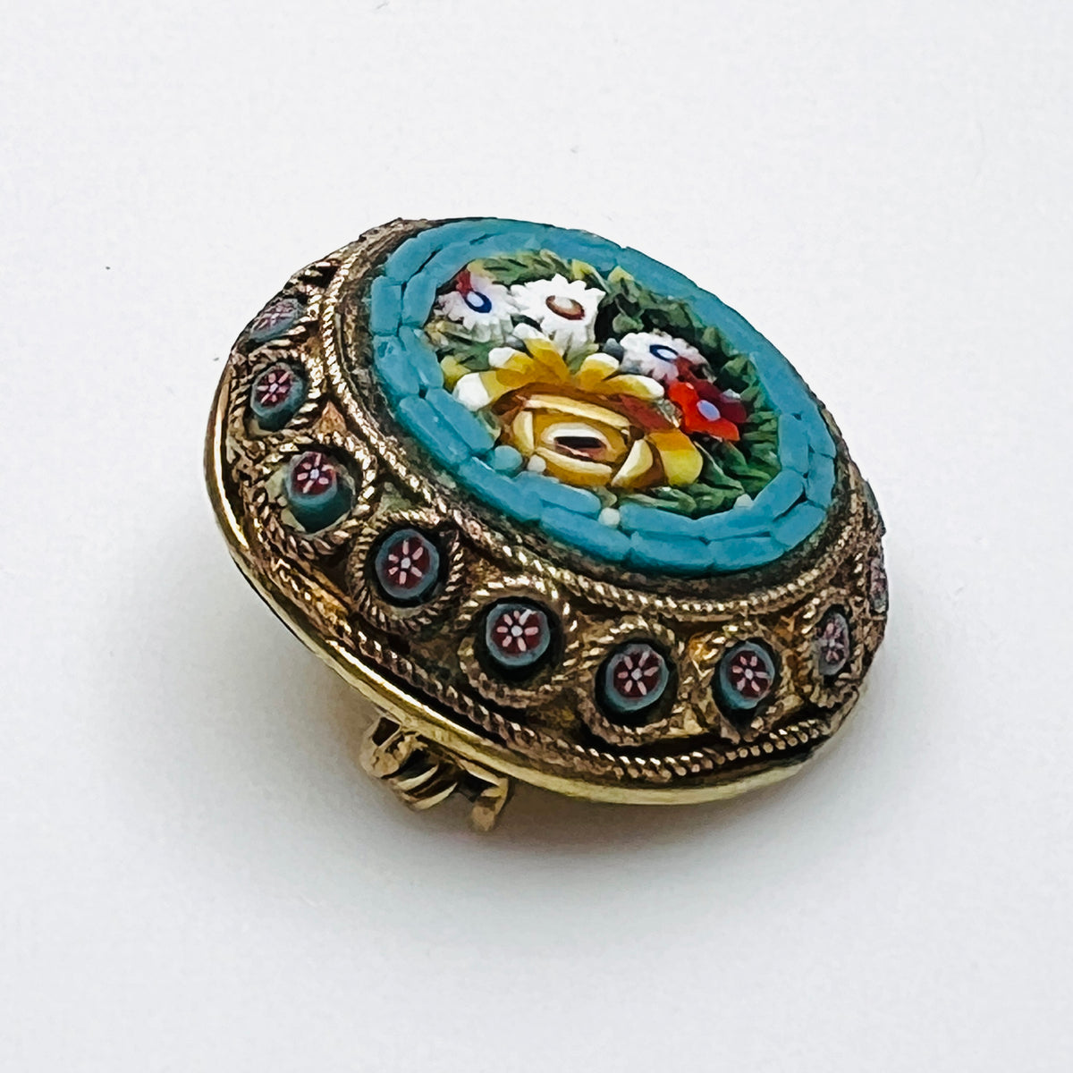 Angled view of floral micro mosaic brooch showing glass tesserae and miniature flower accents around the metal frame.