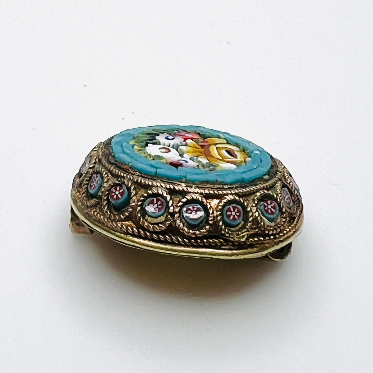 Angled view of floral micro mosaic brooch showing glass tesserae and miniature flower accents around the metal frame.