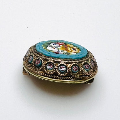 Angled view of floral micro mosaic brooch showing glass tesserae and miniature flower accents around the metal frame.