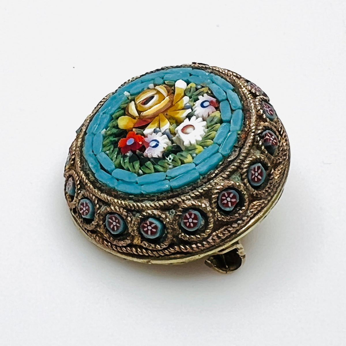 Angled view of floral micro mosaic brooch showing glass tesserae and miniature flower accents around the metal frame.