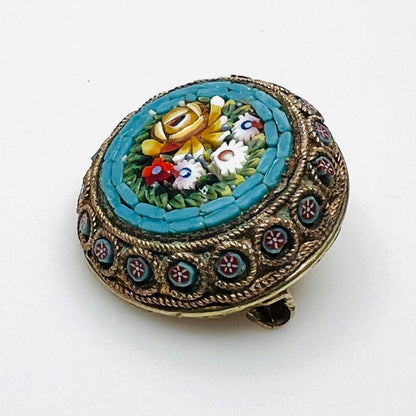 Angled view of floral micro mosaic brooch showing glass tesserae and miniature flower accents around the metal frame.