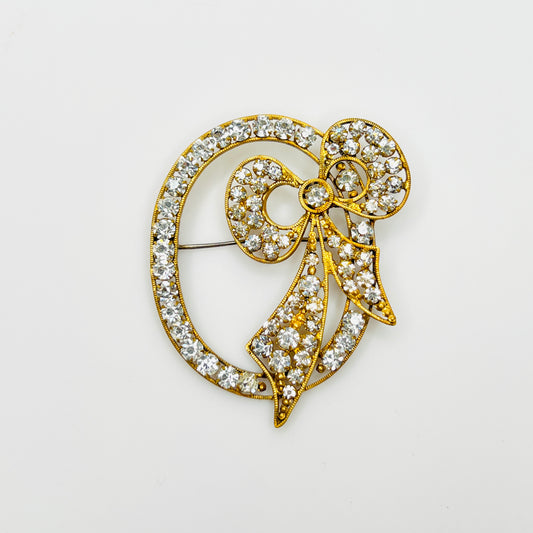 Vintage Czech crystal bow brooch with clear rhinestones, a gold-tone oval frame, and flowing ribbon tails.