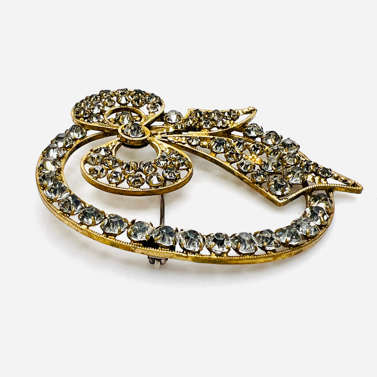Angled view of the gold-tone bow brooch showing raised prong-set clear crystals and ridged borders.