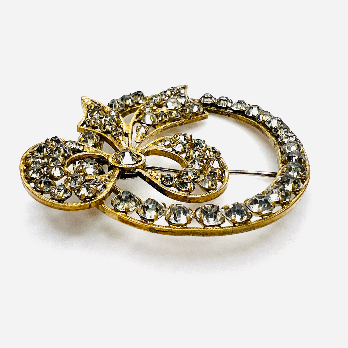 Angled view of the gold-tone bow brooch showing raised prong-set clear crystals and ridged borders.