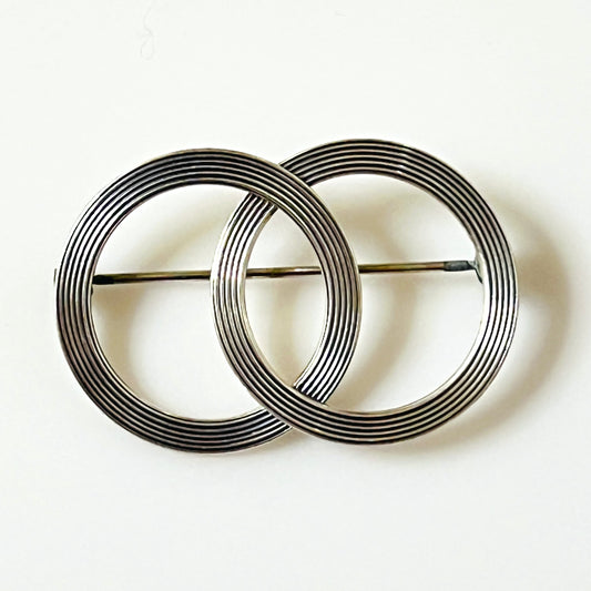 Vintage 1950s Beau sterling silver brooch featuring two overlapping open circles with finely engraved concentric lines in a geometric Modernist design.
