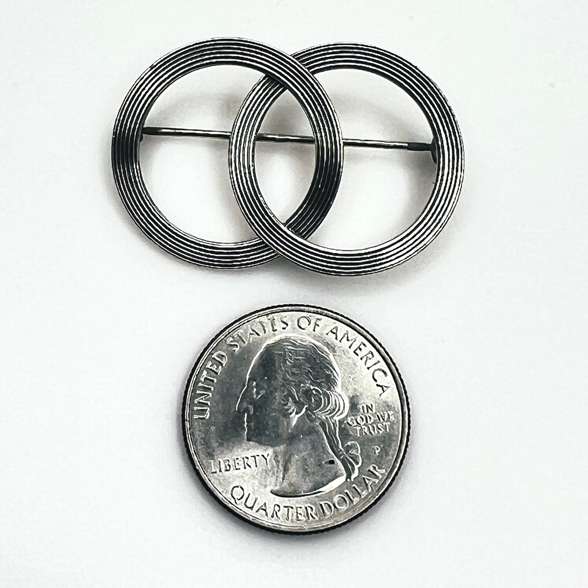 Beau sterling silver double circle brooch photographed beside a quarter for size comparison, showing overlapping rings and linear detailing.