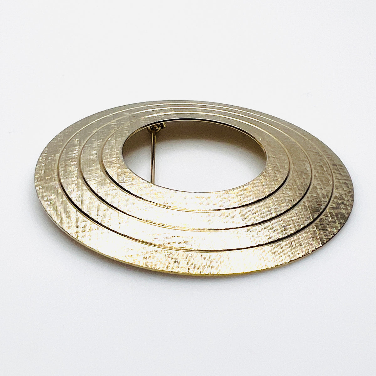 Side view of vintage textured gold tone concentric circle brooch