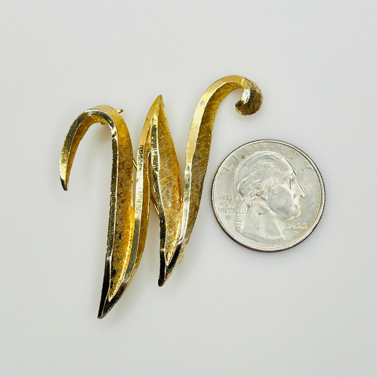 1960s Mamselle gold tone initial M or W brooch shown with quarter for scale