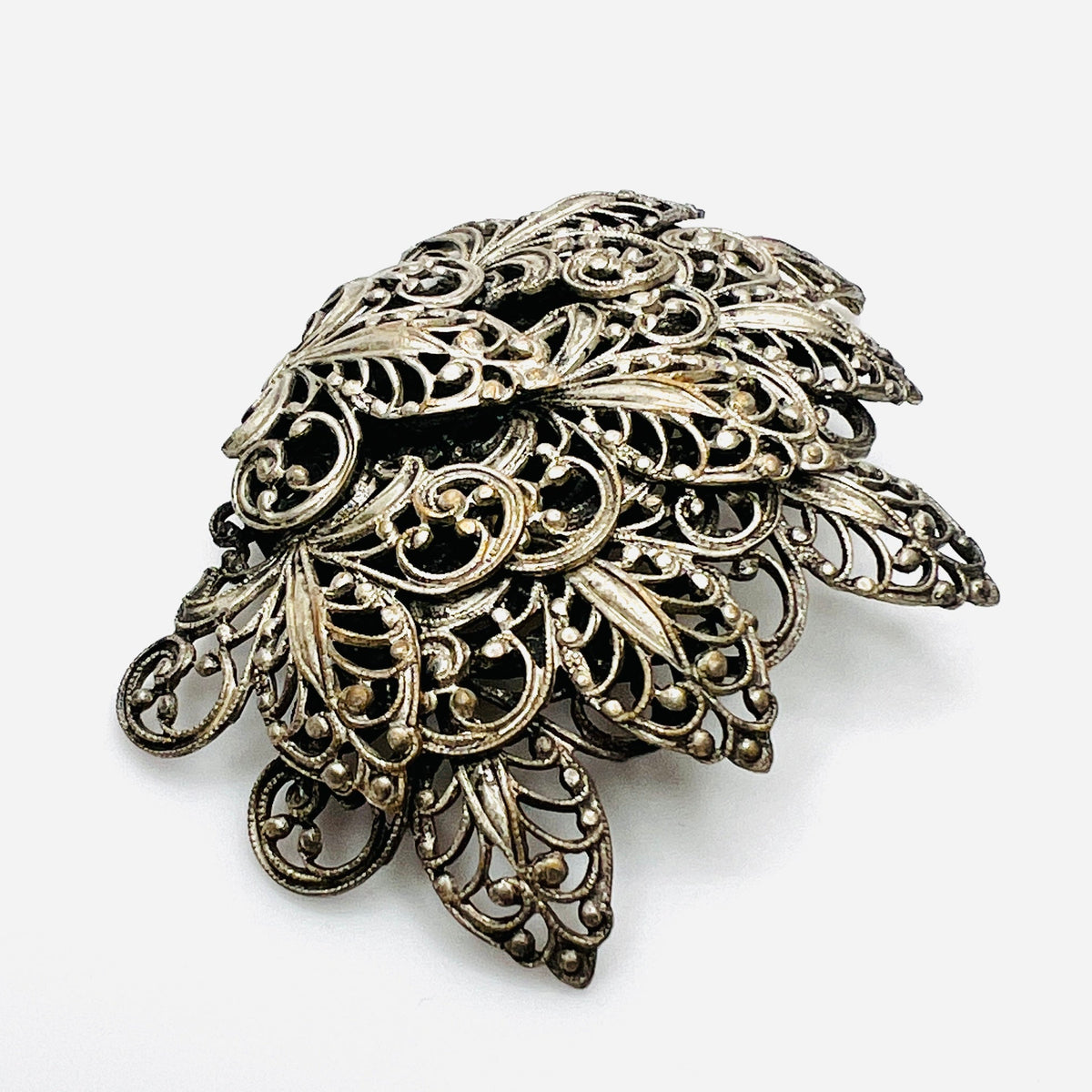 Side view of vintage silver tone filigree brooch showing dimensional layered construction