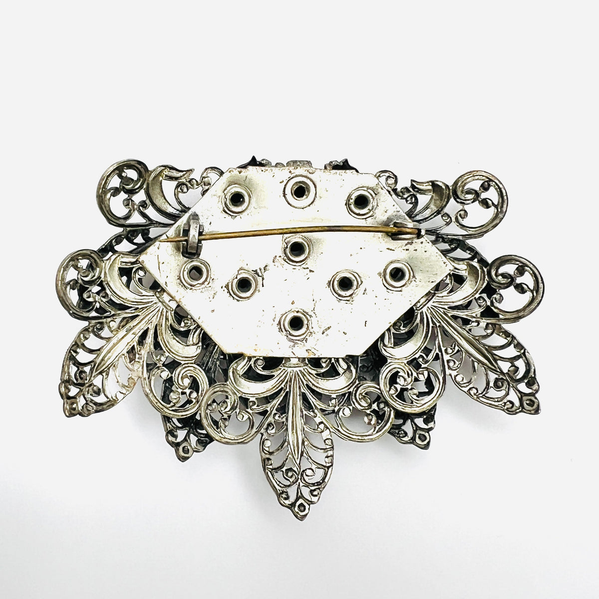 Reverse of 1950s silver tone filigree brooch showing rivet construction and pin closure