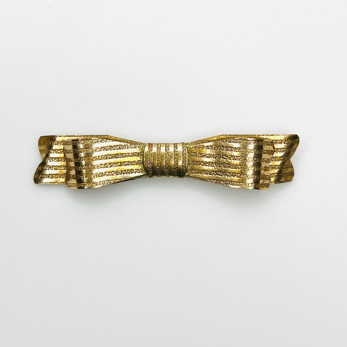 Vintage 1950s gold-tone bow brooch with elongated ribbon shape, textured ridges, and polished accents
