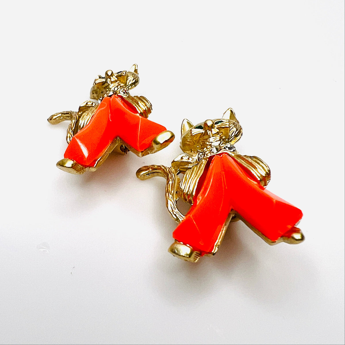 Angled view of two vintage figural cat brooches with dimensional coral Lucite trousers