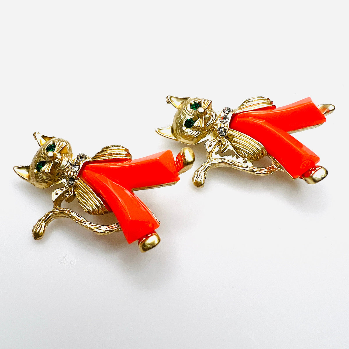 Angled view of two vintage figural cat brooches with dimensional coral Lucite trousers