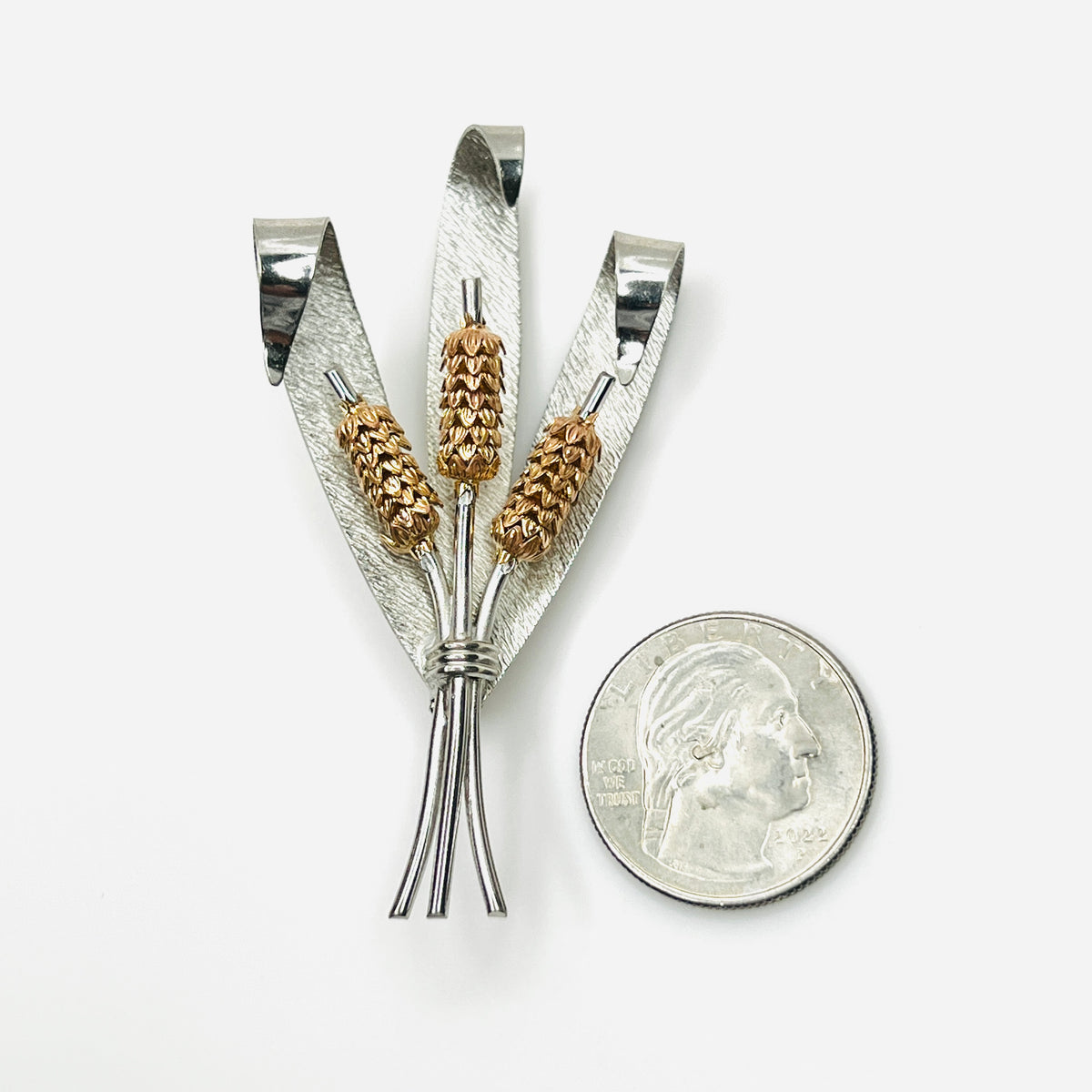 1950s gold and silver-tone cattail brooch shown beside quarter for scale