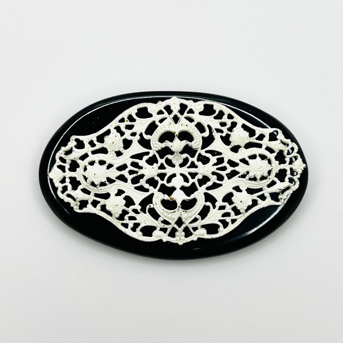 Vintage 1950s oval brooch with ornate white enamel floral filigree over a glossy black base